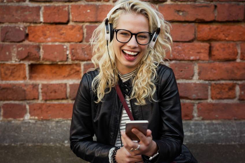 Una mujer consume contenido de audio digital con smartphone y auriculares