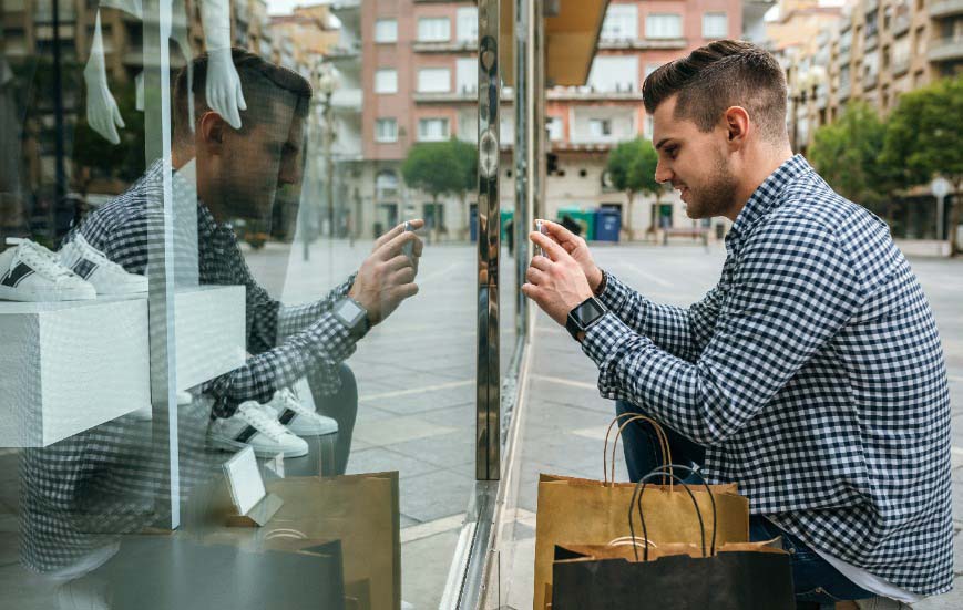 Un hombre saca una fotografía de unas zapatillas en un escaparate para utilizarla en Visual Search