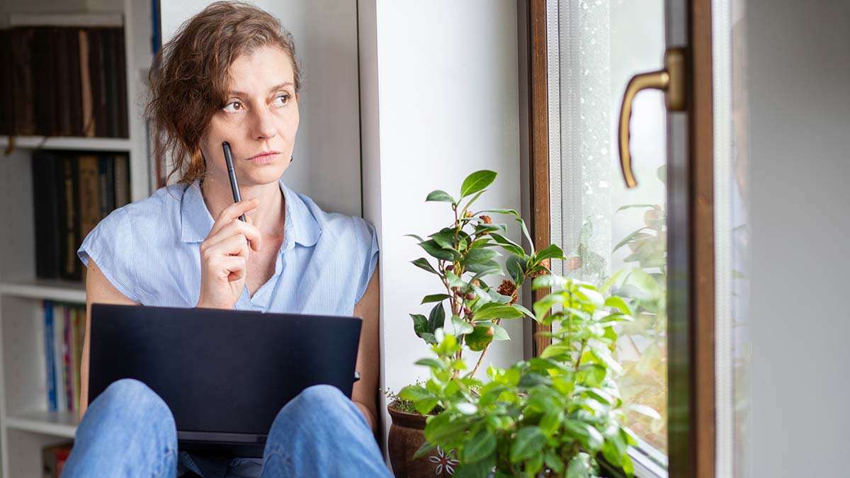 Mujer pensativa trabajando con el ordenador junto a la ventana